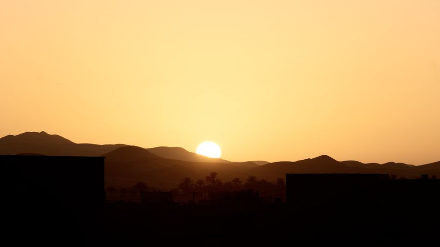 The sun setting behind a dark mountain ridge