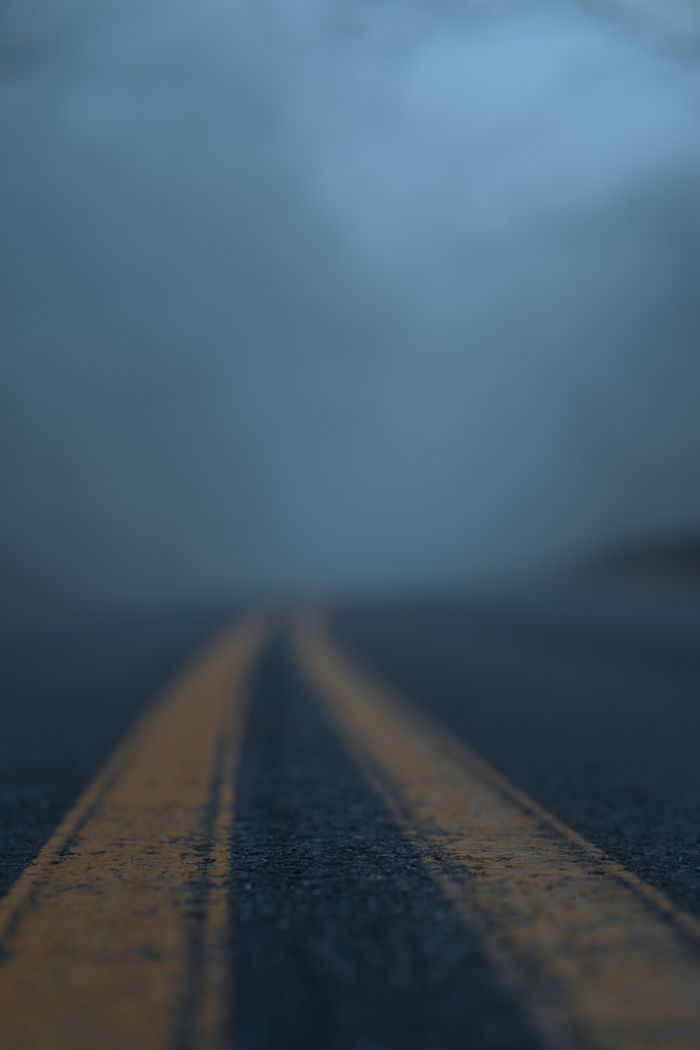 A two-lane road disappearing into blue fog