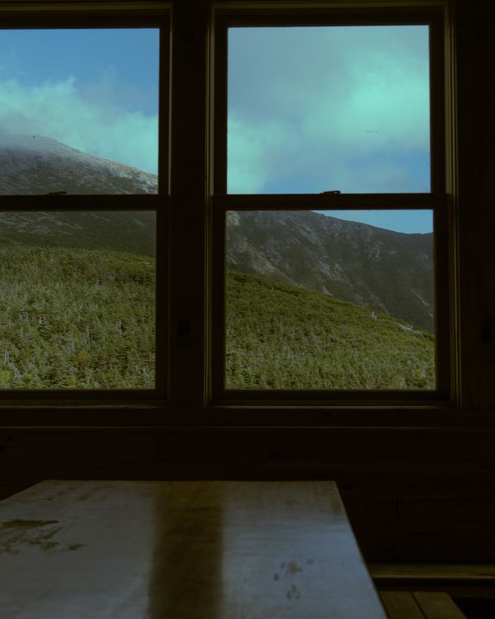 A dark cabin interior, windows looking out onto a green mountainside